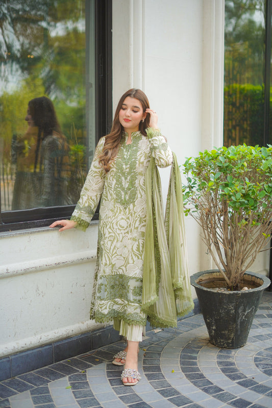 Woman in a green and white traditional outfit standing by a window with a plant in the foreground.