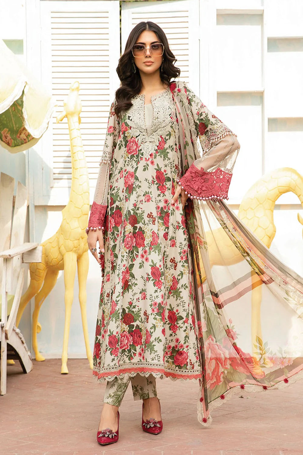 Woman in a floral dress with a sheer dupatta in a decorated room.