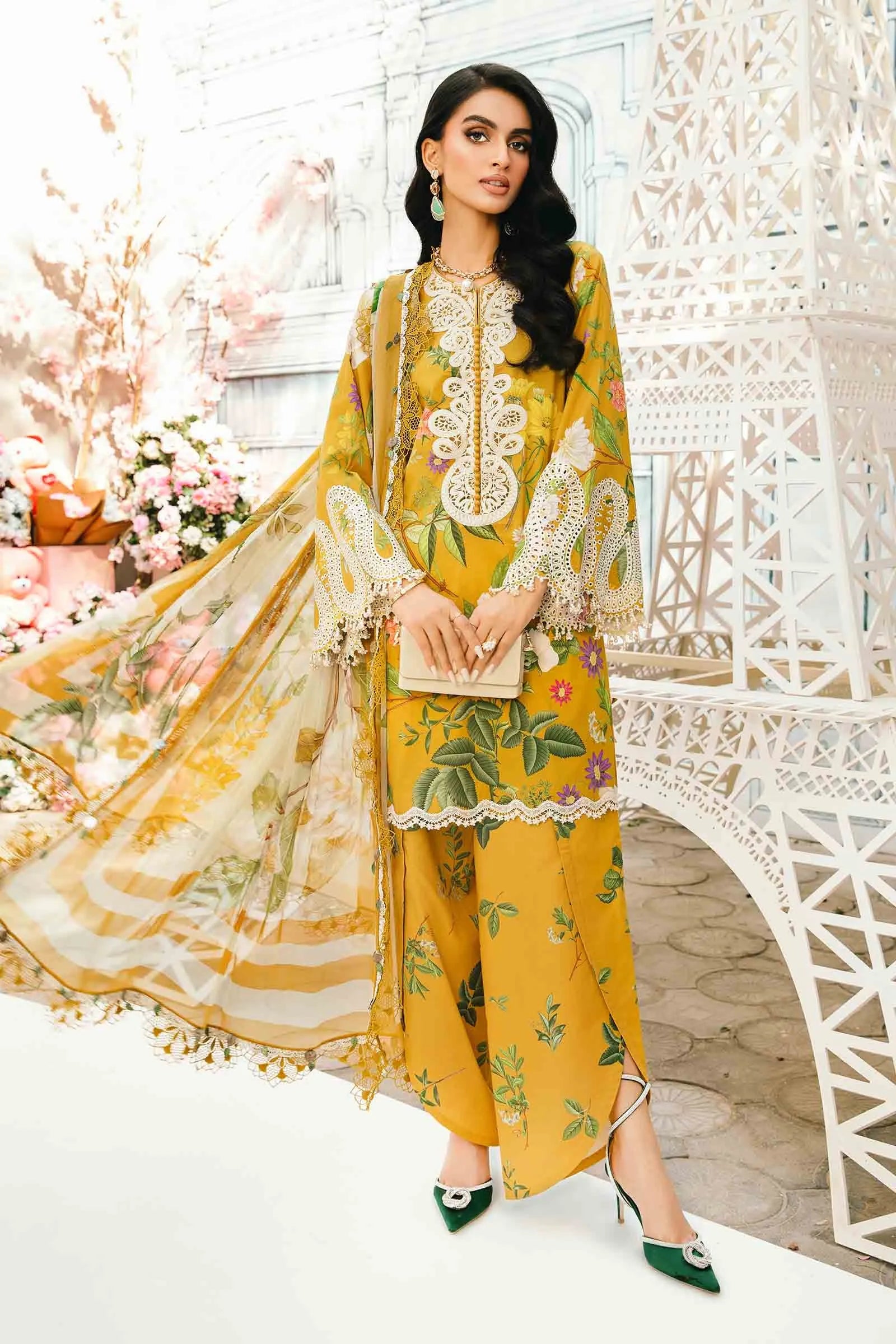 Woman in a yellow and green traditional outfit with floral patterns, standing in a decorative indoor setting.