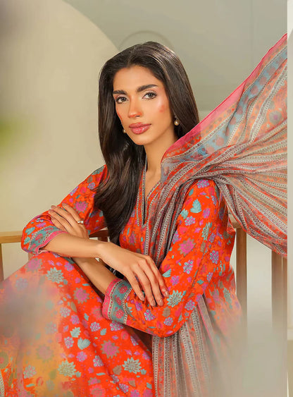 Woman in a vibrant orange traditional outfit with floral patterns, sitting indoors.