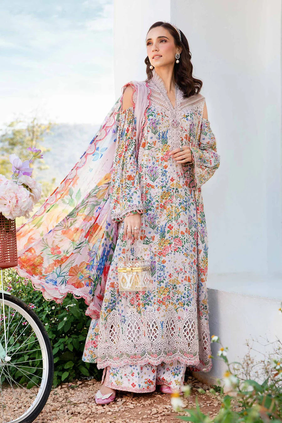 Woman in a floral traditional outfit standing outdoors with a bicycle and flowers in the background