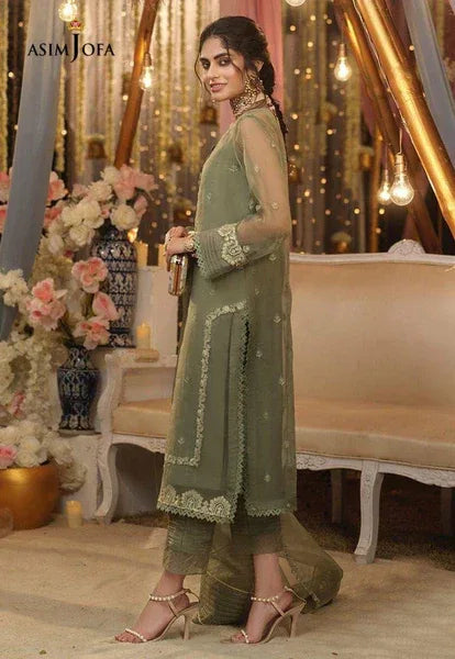 Woman in a green traditional outfit standing in an elegant indoor setting with decorative elements.