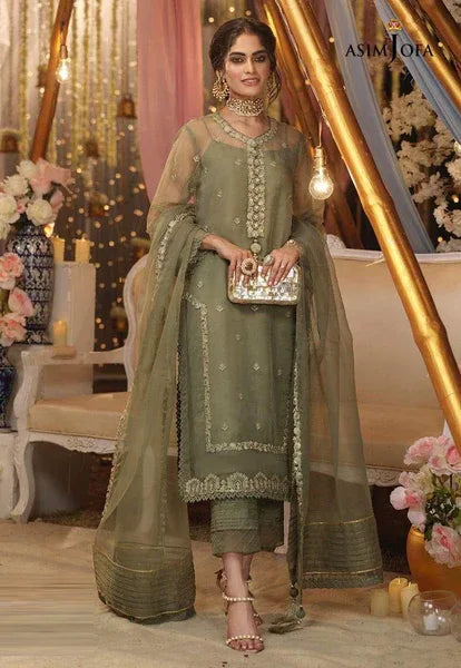 Woman in a green traditional outfit with jewelry and a clutch, standing in a decorated indoor setting.