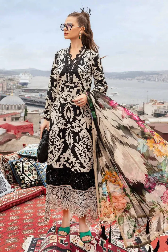Woman in a black and white patterned dress with a colorful floral coat, standing on a rooftop with a cityscape in the background.