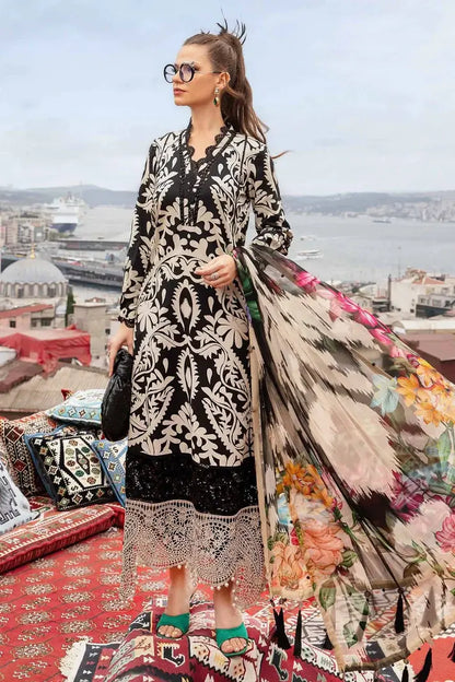 Woman in a black and white patterned dress with a colorful floral coat, standing on a rooftop with a cityscape in the background.